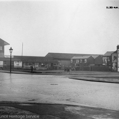 Street corner with the football ground and a large advertisement for C&S XL Ales on the side of the stand.