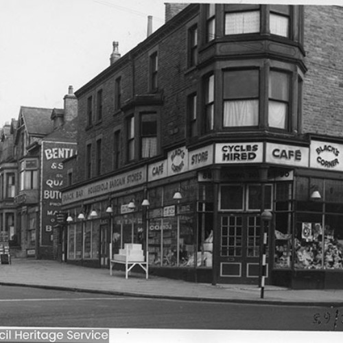 Street corner, with the shop fronts of Black's Corner Store and Cafe with Bentley and Son Butchers next door to the left.