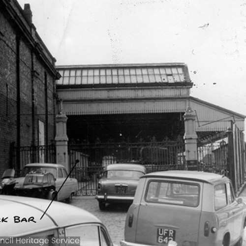 Cars parked up outside a gated area of the building. There is handwriting on the image which says Snack Bar and a direction line that points inside the building.