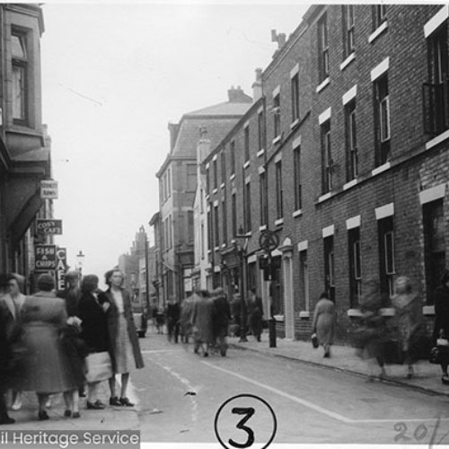 People walking on the street past a number of businesses including the Stanley Arms public house, the Cosy Cafe and an Outfitters shop.