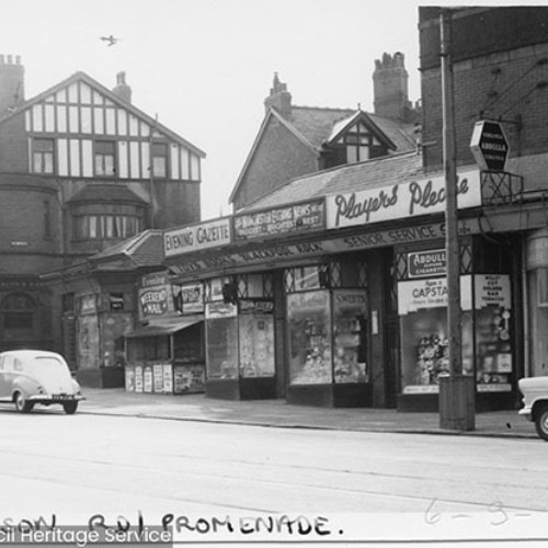 Shop fronts advertising the Evening Gazette, Blackpool Rock and gifts. On the left is the corner of a William Deacon's Bank.