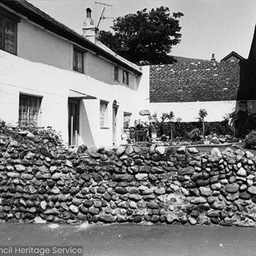 Three white-washed terraced cottages behind a cobblestone wall.