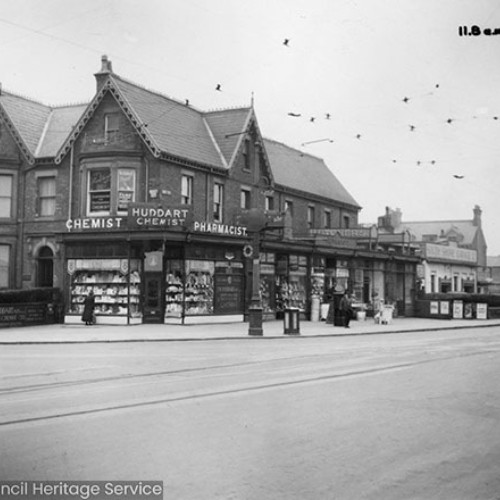 Street corner with shop fronts, including Huddart Chemist on the corner.