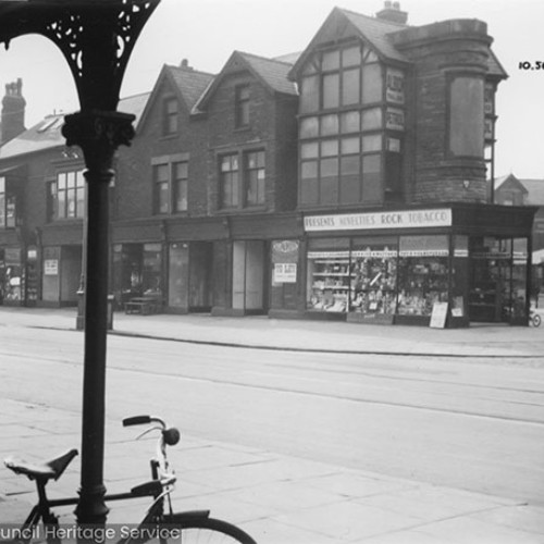 Row of shop fronts, with the shop on the street corner advertising presents, novelties, rock and tobacco.