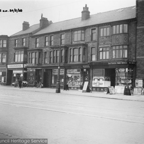 Row of shop fronts, including Collinsons and a bicycle shop, which has a number of bicycles out on their forecourt.