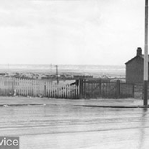 The road, with Squires Gate Holiday Camp and the sea in the distance. There are also a couple of houses to the right.