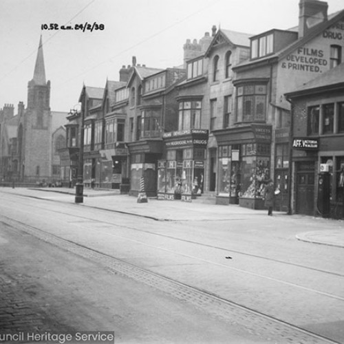 Shop fronts including South Pier Garage and Premier Drug Store, with a church further up the street.