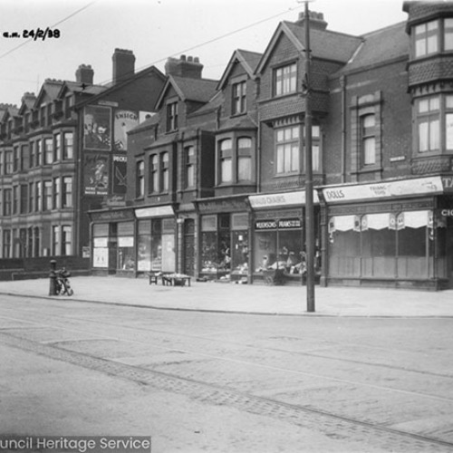 Shop fronts to the right, including Taylors on the corner and large houses on the left.