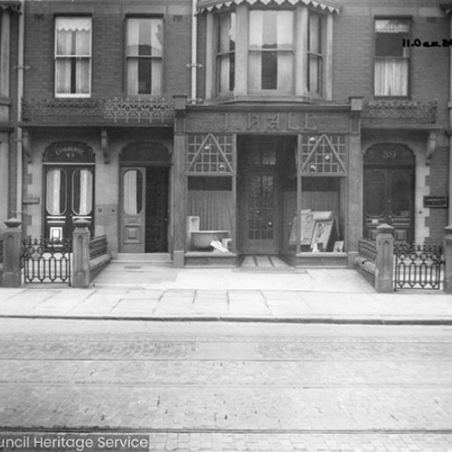 Exterior of adjoining buildings, with the business of J. Hall advertised on the shop front in the centre.