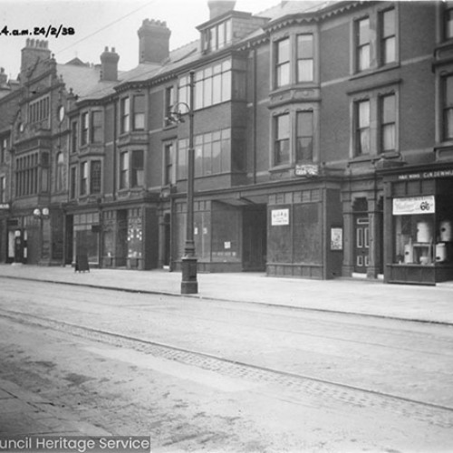 Row of buildings, some of which are shops, with the Grand Hotel and a sign for Taxis to the left.