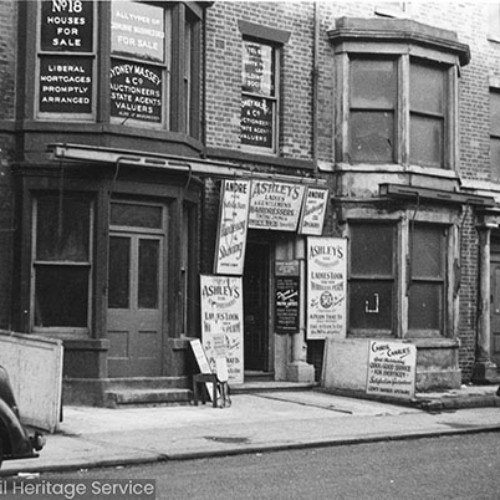Shop front with the ground floor advertising hairdressers Andre and Ashley's and the upstairs advertising Sydney Massey and Co Auctioneers, Estate Agents and Valuers. To the right is another shop front advertising a tailors and Ben-Vic rugs.