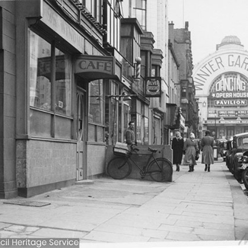 The Windmill Cafe and a row of shops leading up to the Winter Gardens, which is advertising Dancing, Opera House, Pavilion.