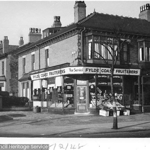 Street corner, with the Fylde Coast Fruiterers shop on the corner with boxes of fruit on the outside of the shop.