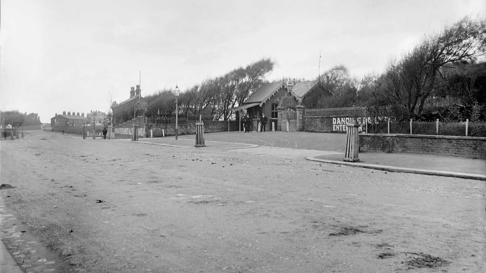 Street scene of a road with a small kiosk and entrance gates to gardens