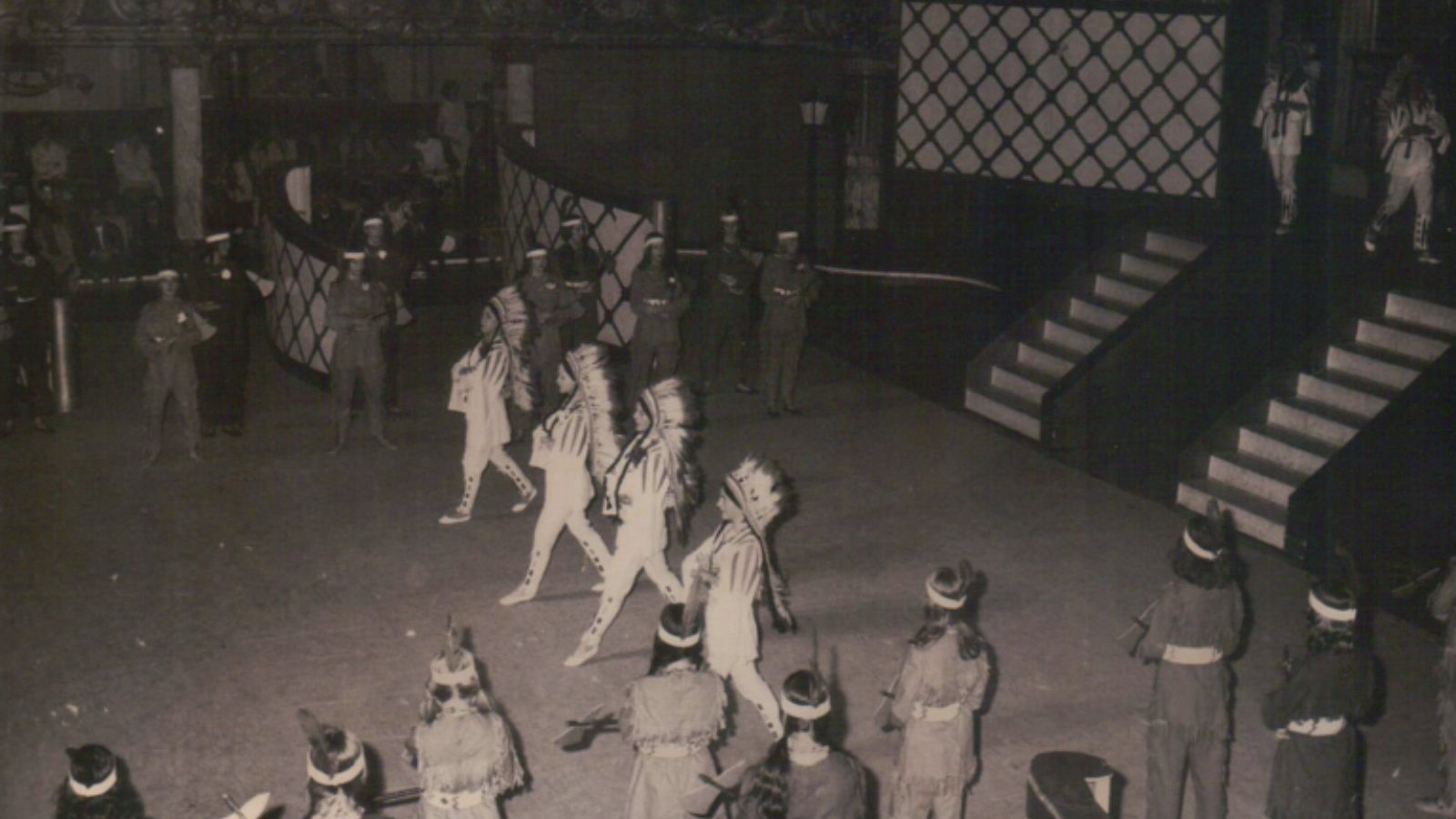 A group of dancers performing on a stage, wearing Native American inspired costumes.