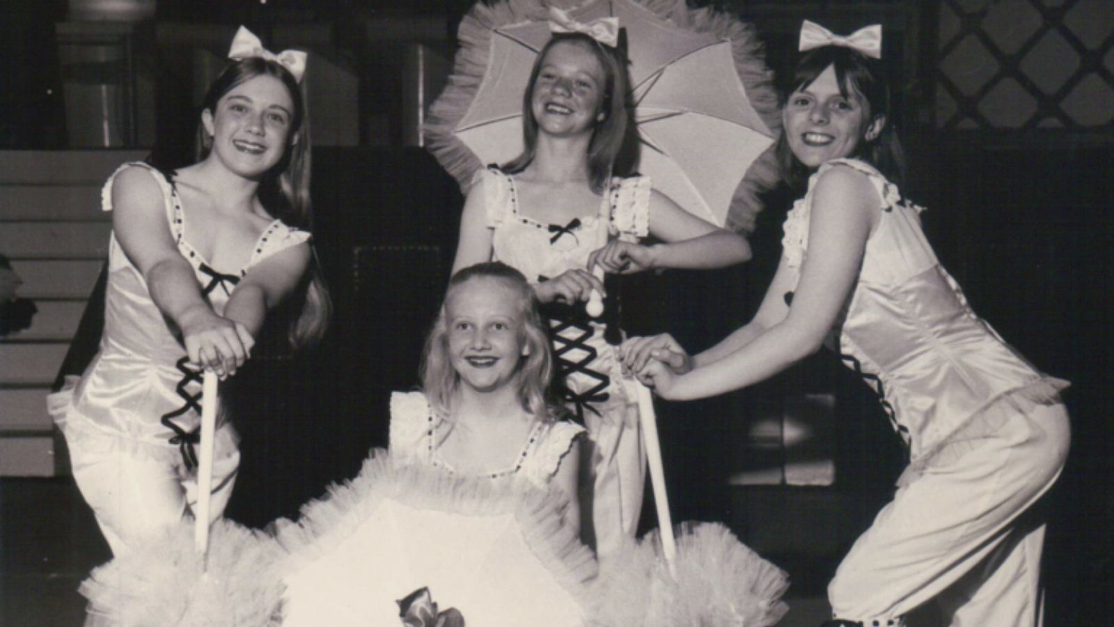A group of four girls posed in a group holding parasols.