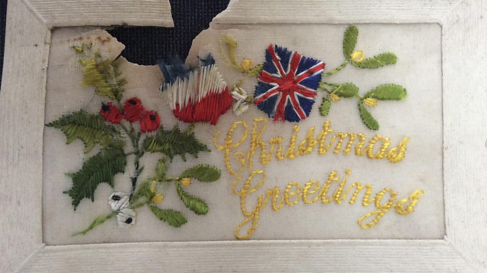 A hand stitched Christmas card with holly and ivy motif and British and French flags.