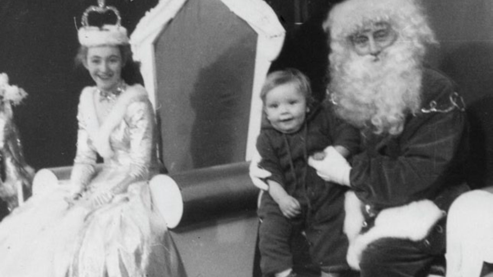 A Queen and Santa Claus sat on thrones, Santa has a child on his knee.