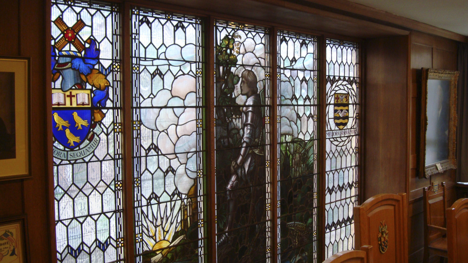 A stained glass window with crests and a depiction of a knight in armour.