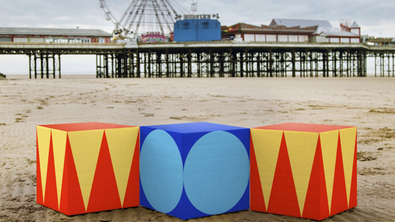 Three Showtown branding blocks spelling 'Wow' sat on the beach, in front of the pier.