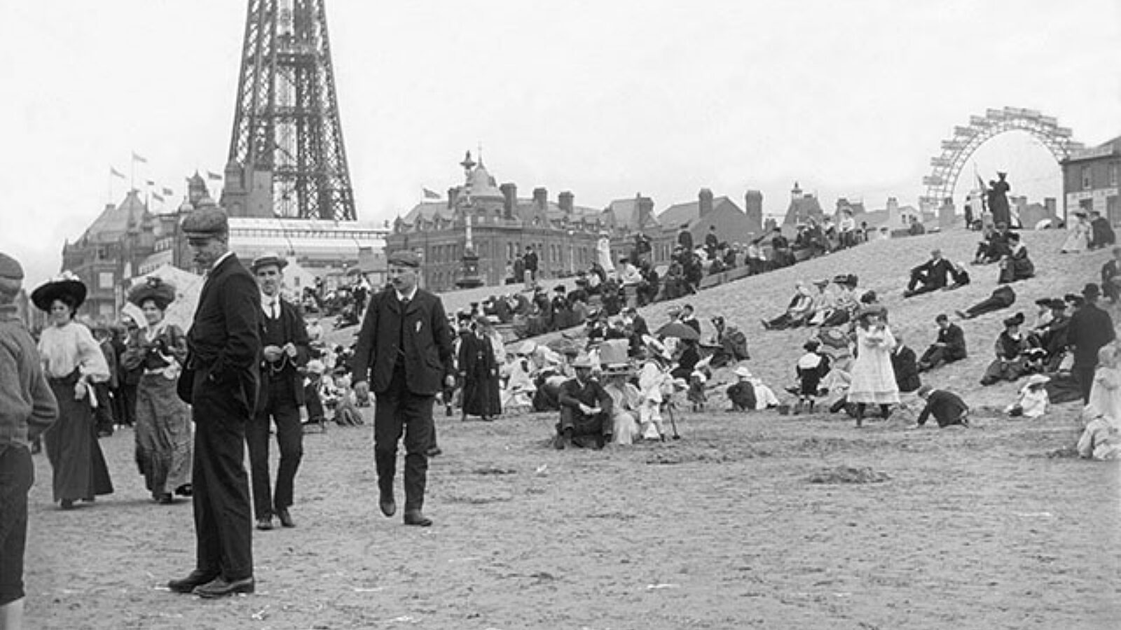A black and white image with well dressed people walking on the beach