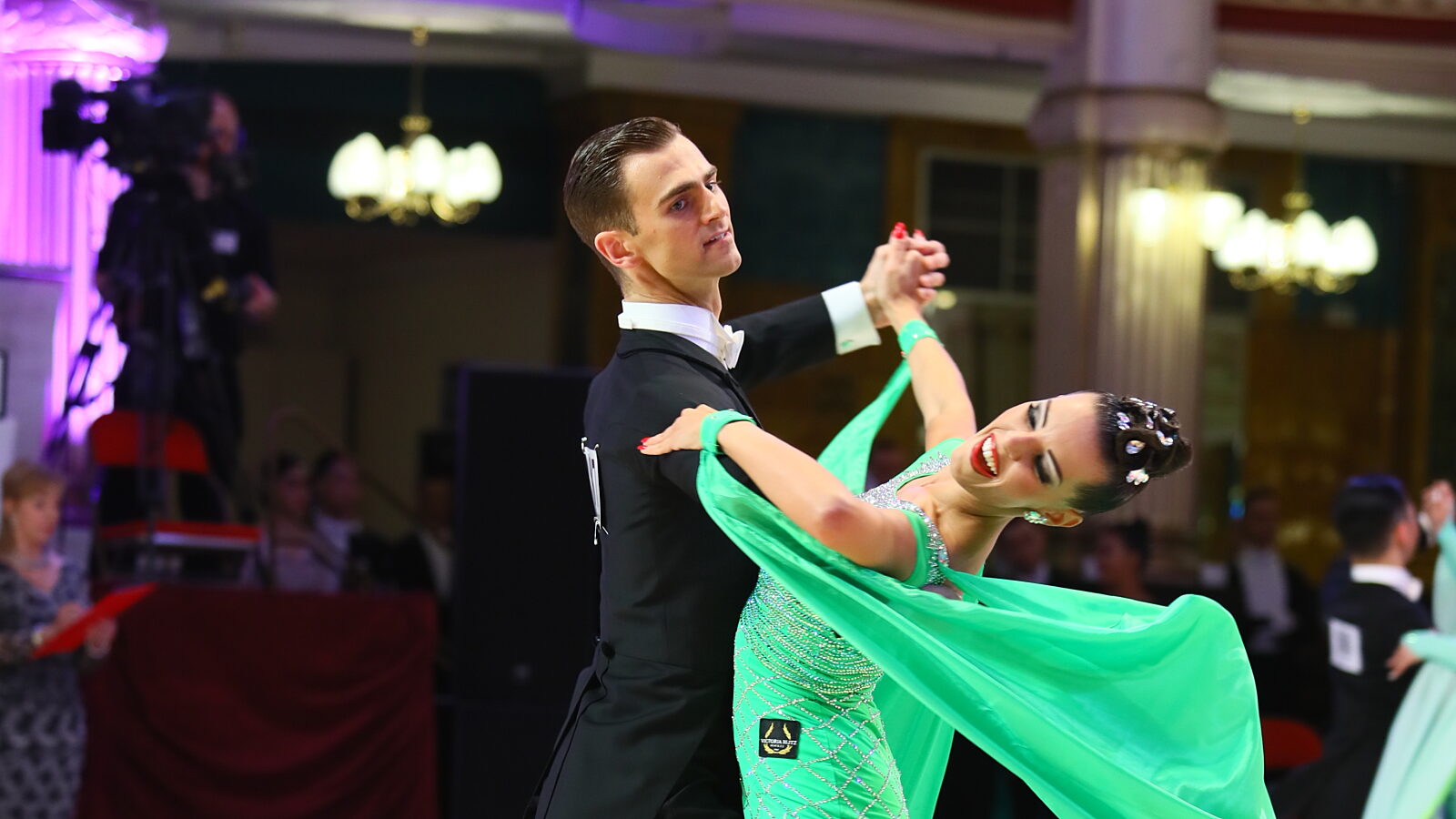Two ballroom dancers dancing wearing a green dress and suit.