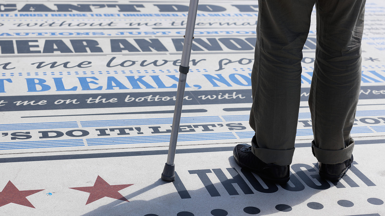 A photograph of legs and a walking stick, standing of the comedy carpet.