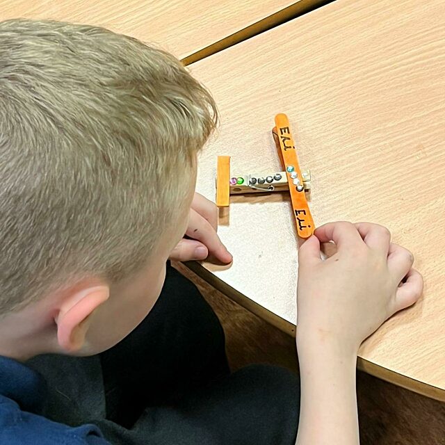 Boy making a plane from lolly sticks and pegs