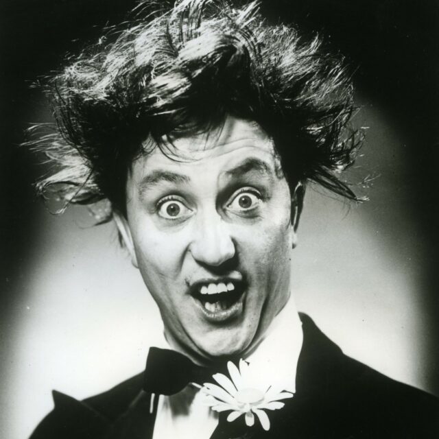 Black and white image of Ken Dodd. Head and shoulders shot.