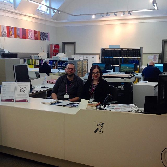 Heritage Assistants, Tom and Hayley sat at the History Centre desk smiling.