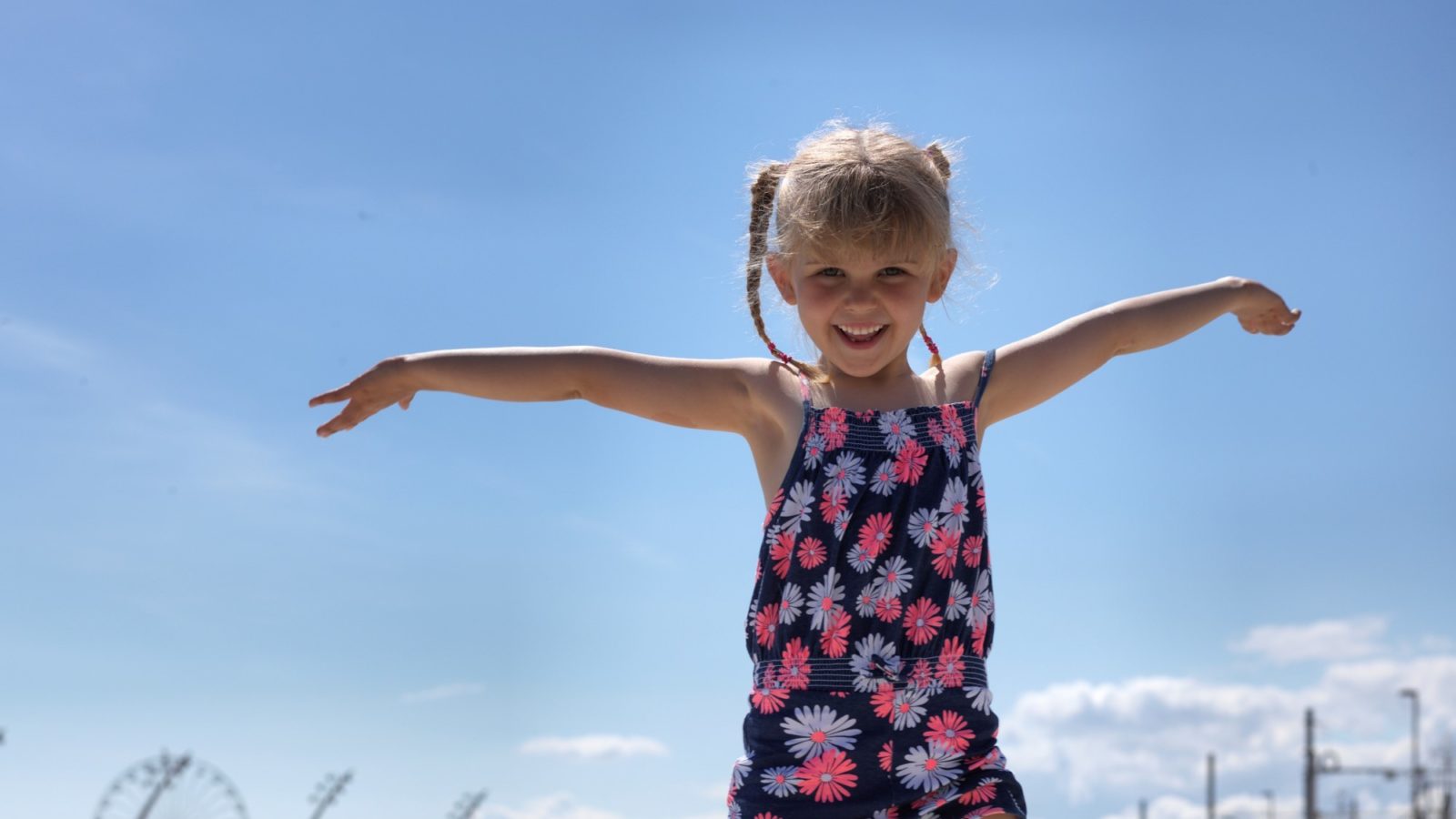 Small girl with her arms stretched out wide against a bright blue sky.