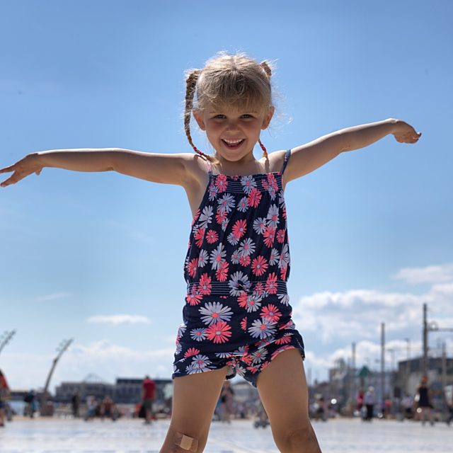 Small girl with her arms stretched out wide against a bright blue sky.