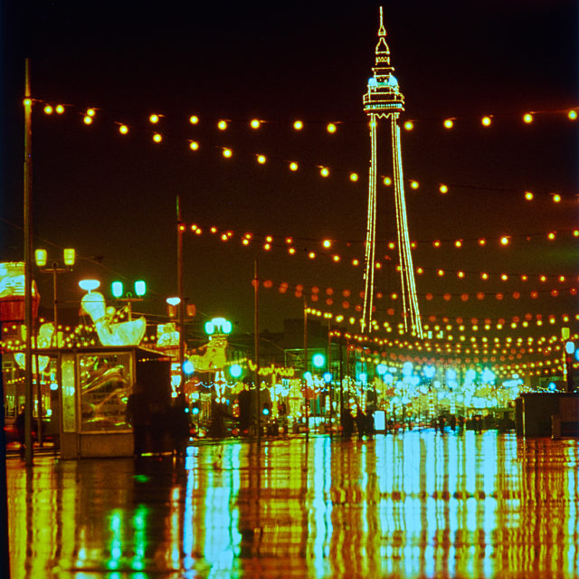 A view of the illuminations and tower, with lights reflecting off the wet ground.
