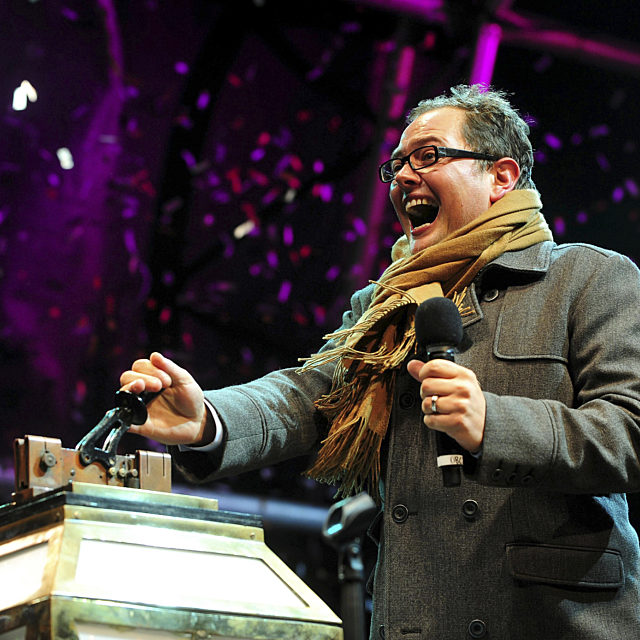 Alan Carr in coat and scarf pulling the illuminations switch on switch
