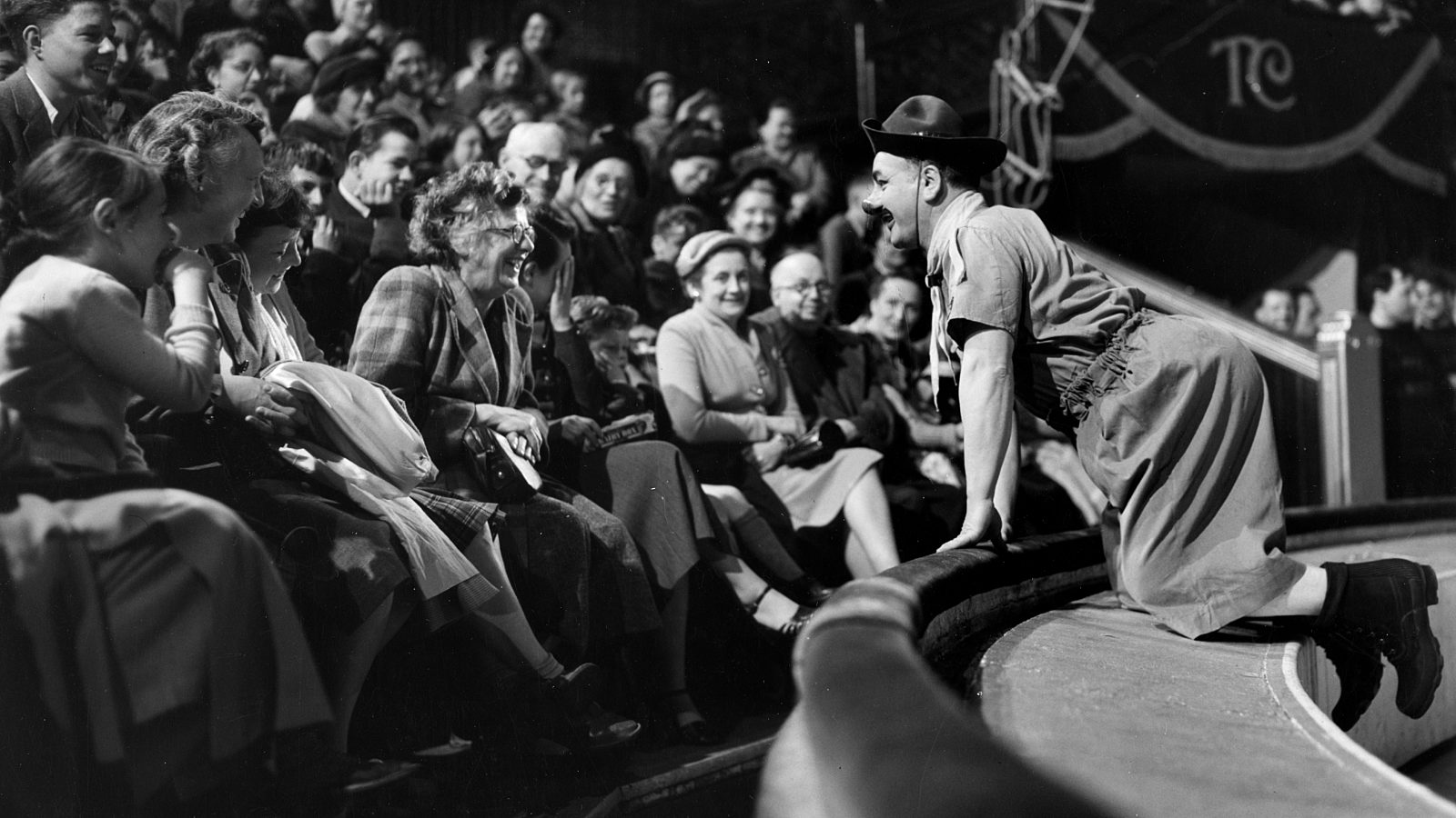 Black and white photograph of Charlie Cairoli leaning into the circus audience