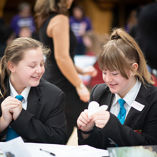 High school children sat at a table smiling whilst engaging in an activity