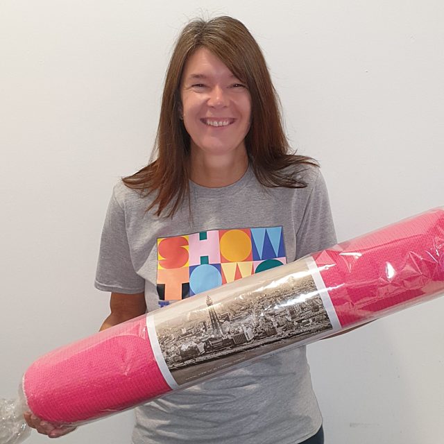 Rachel smiling holding a large stick of Blackpool rock and wearing a showtown t-shirt.