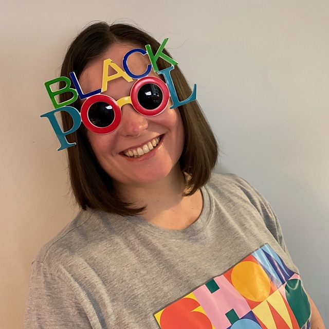 Emma smiling, wearing a Showtown t-shirt and Blackpool sun glasses.
