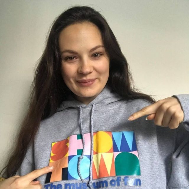 Laura wearing a Showtown top, smiling and pointing at the logo.