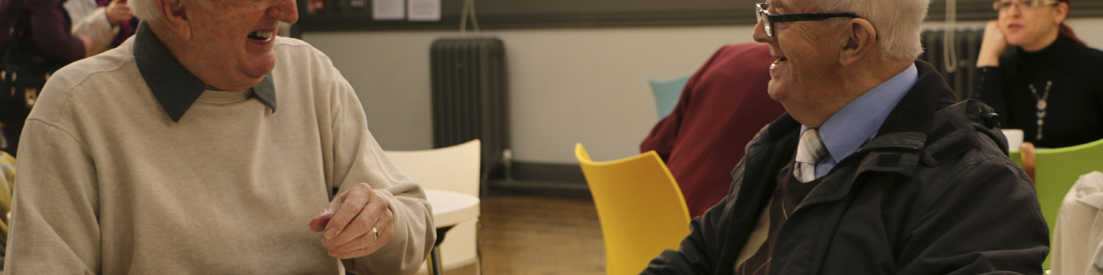 Two volunteers sat at a table each with a cup of tea laughing together