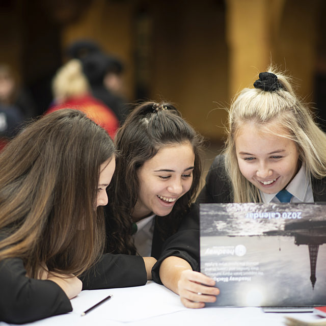 Three smiling girls sat at a table, looking at a photograph