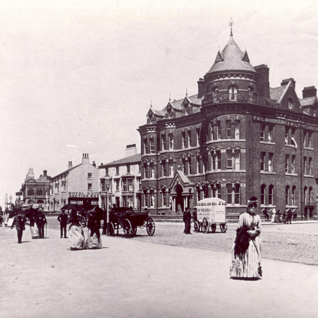 Victorian photo of people walking down the prom with the Palatine building behind.