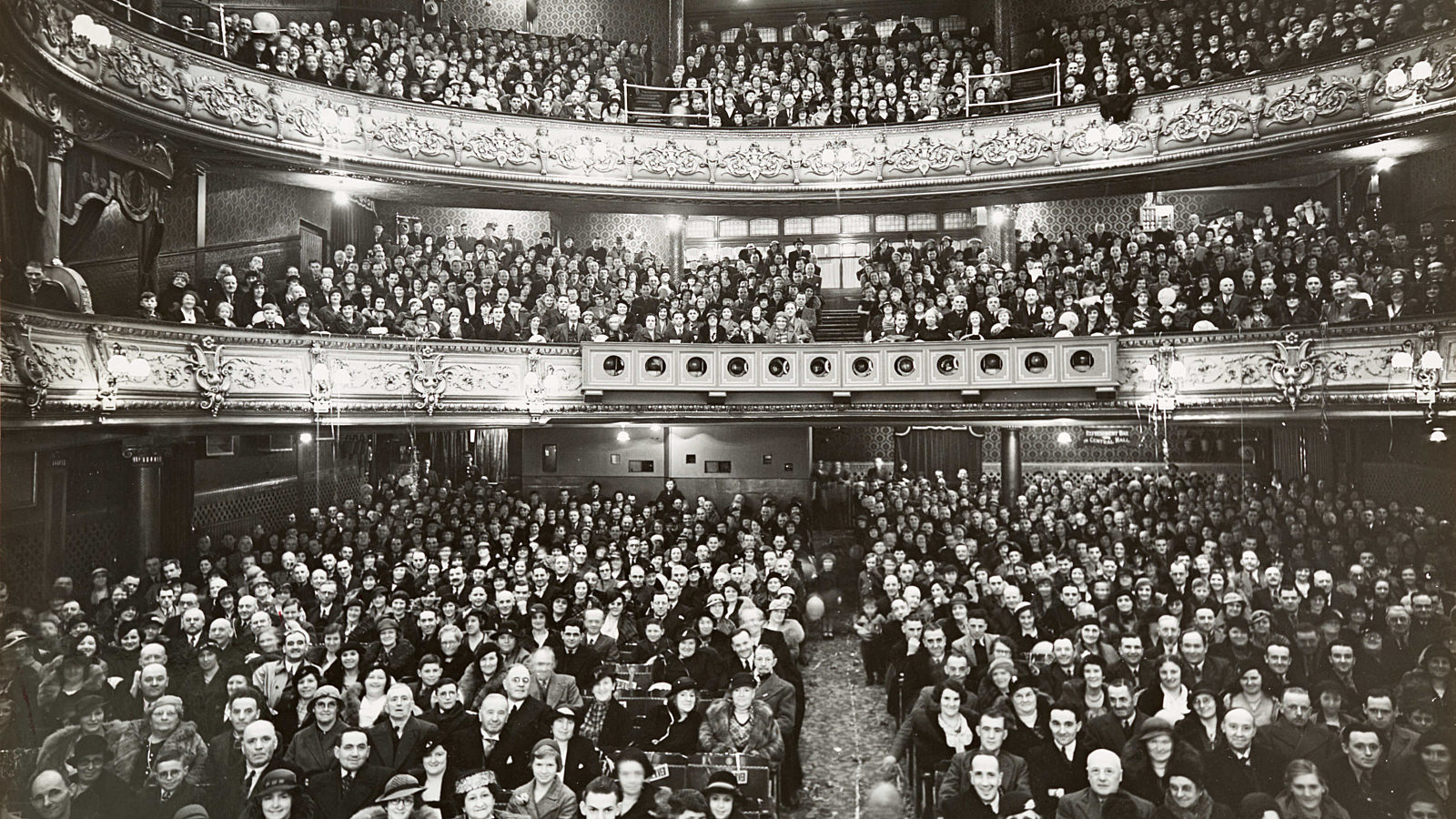 A black and white photo of a crowded theatre audience, taken from the stage