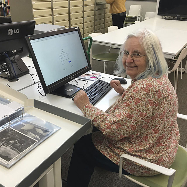 Smiling volunteer sat at a computer with collection photographs