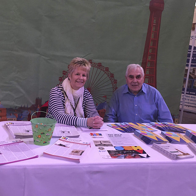 Two volunteers sat smiling at a desk full of leaflets