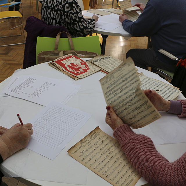 Two volunteers, one looking at sheet music and the second writing.