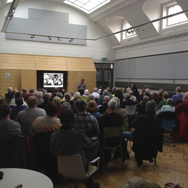 A crowed room filled with people watching a video