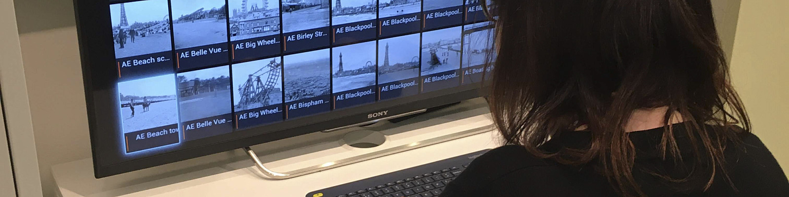 Person sat in front of a computer screen full of black and white photographs.