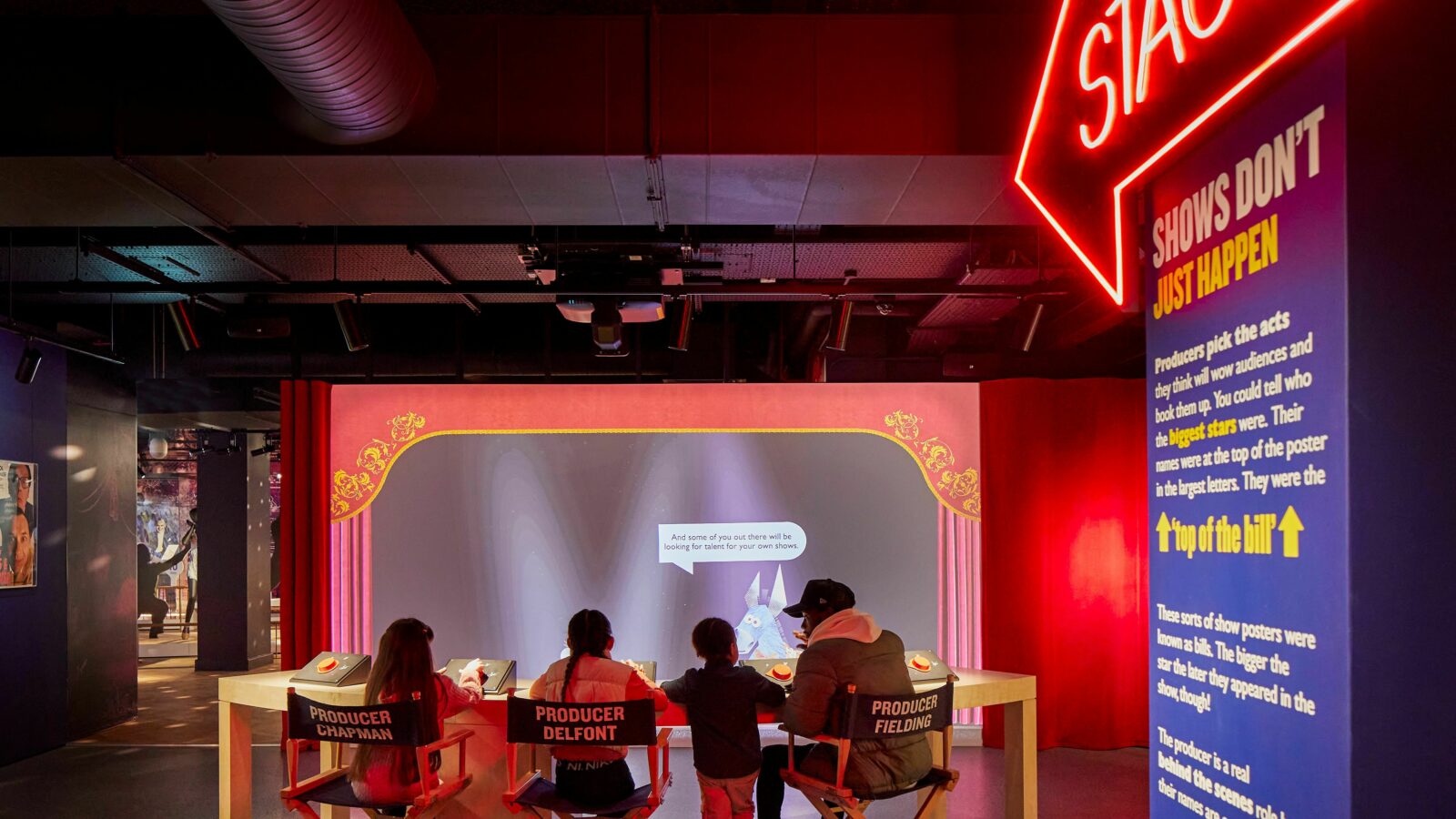 Inside the Showtime gallery at Showtown.  A neon sign points to the stage and a family are sat in 'directors chairs' loooking at a screen.