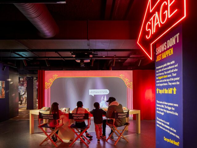 Inside the Showtime gallery at Showtown.  A neon sign points to the stage and a family are sat in 'directors chairs' loooking at a screen.